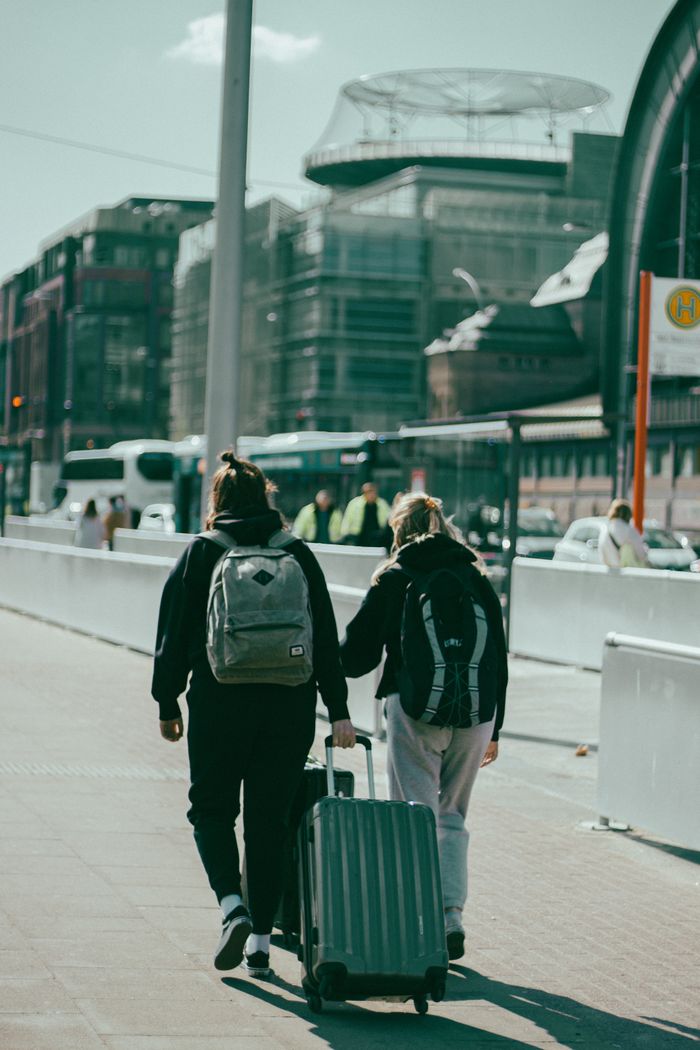 why-choose-us A couple of travelers walk through a sunlit city, dragging their suitcase on the sidewalk.