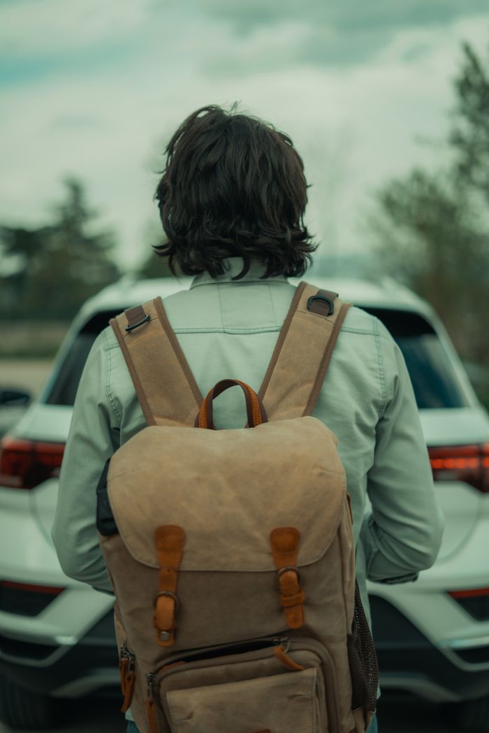 journey Back view of a traveler with a backpack standing in front of a white car, outdoors.