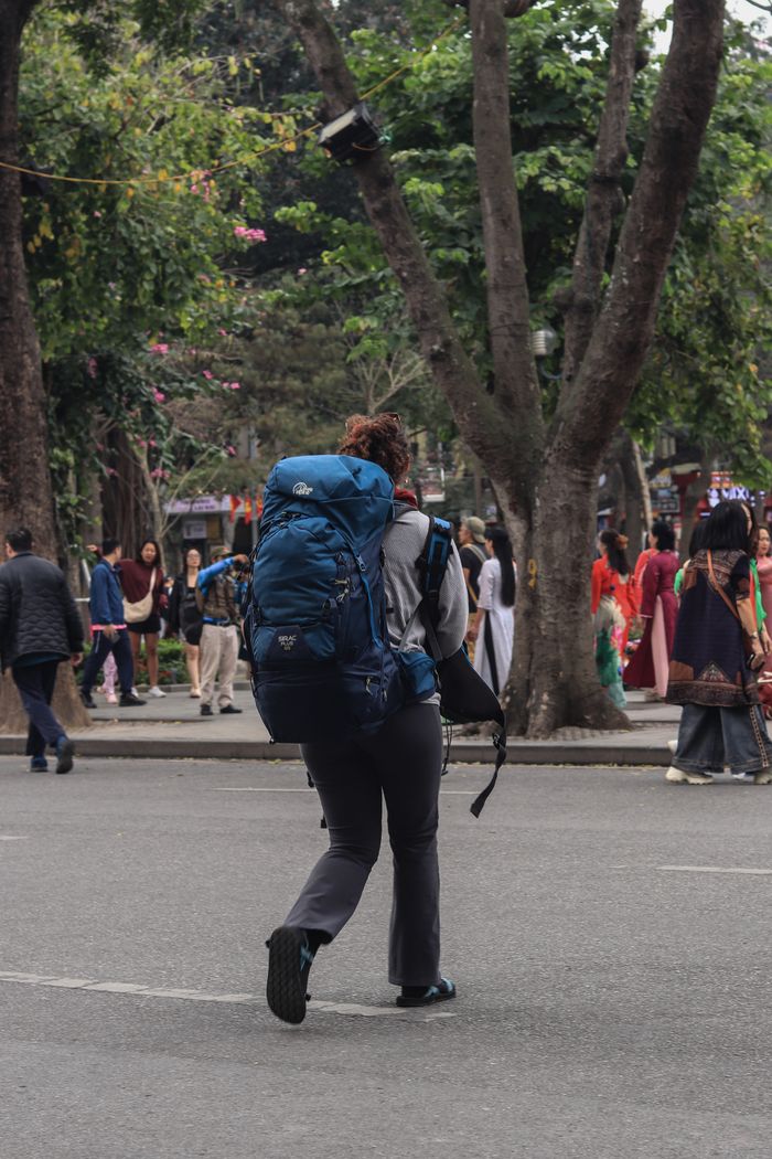 services-03 A traveler with a large blue backpack walks through a bustling city street filled with people and trees.