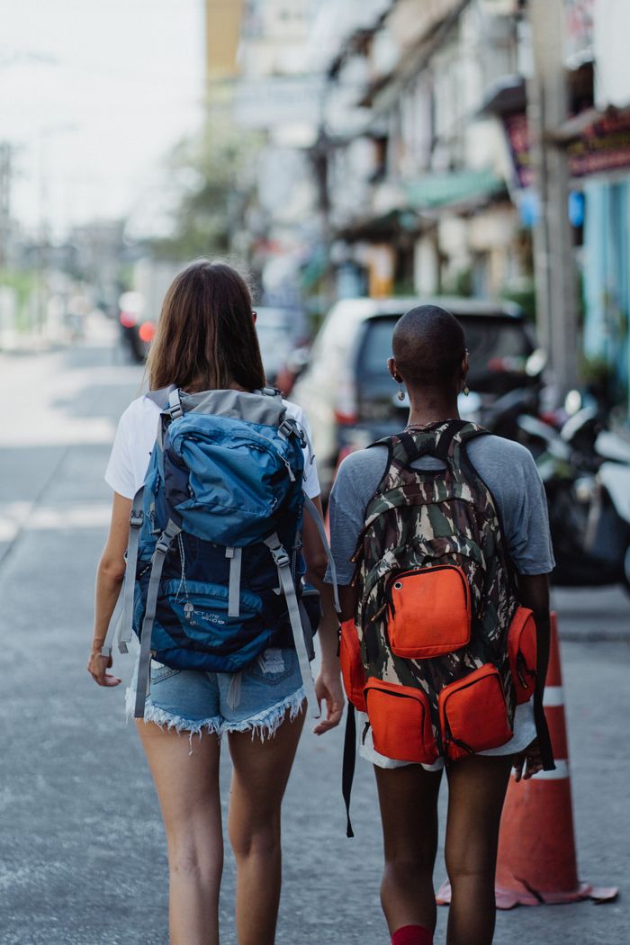 services-02 Two women with backpacks walk through an urban street, capturing the spirit of adventure and exploration.