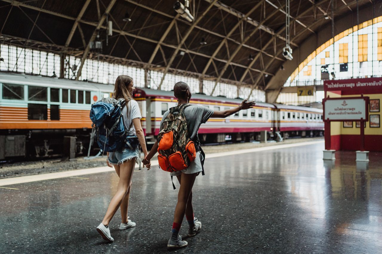 team-02 Two women with backpacks walking through a train station, showcasing adventure and friendship.