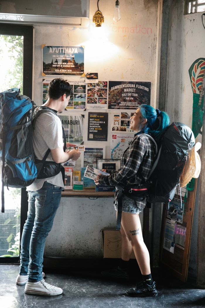 who-we-are Two backpackers examining maps and brochures inside a travel information center.