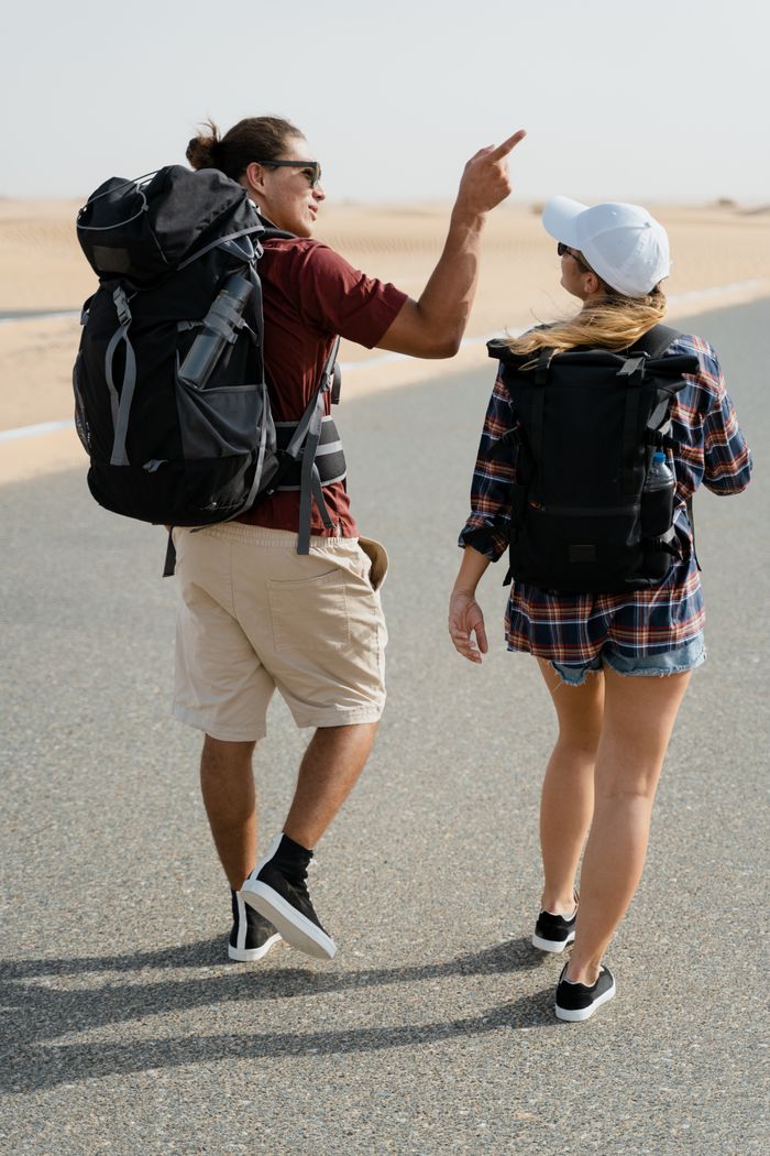 services-04 Couple walking on a desert road with backpacks, discussing their adventure.